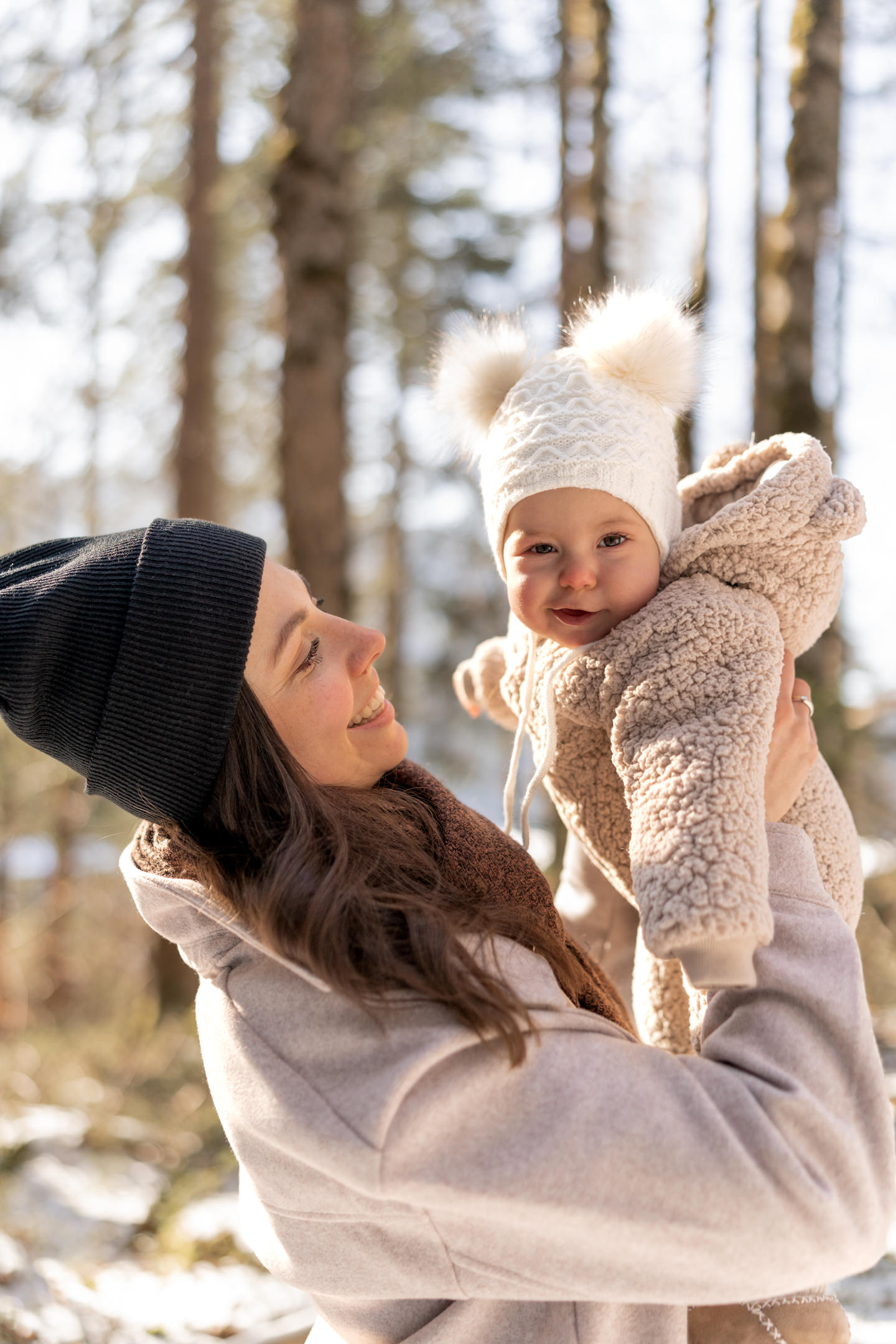 Mutter und Tochter lachen sich während eines Familienshootings am Eibsee im Winter an und die Sonne leuchtet durch die Bäume