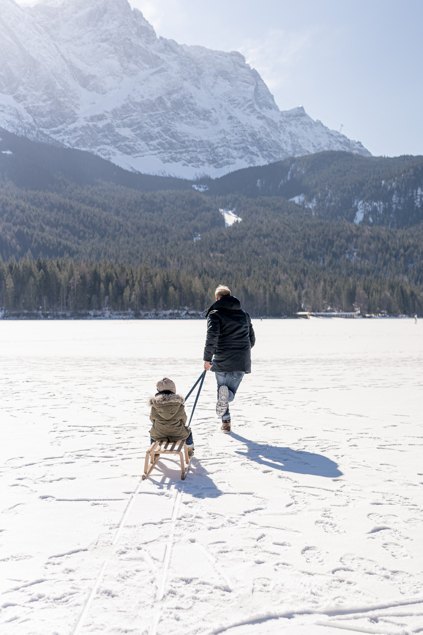 Vater und Sohn rennen mit Schlitten über den Eibsee im Winter bei einem Familienshooting