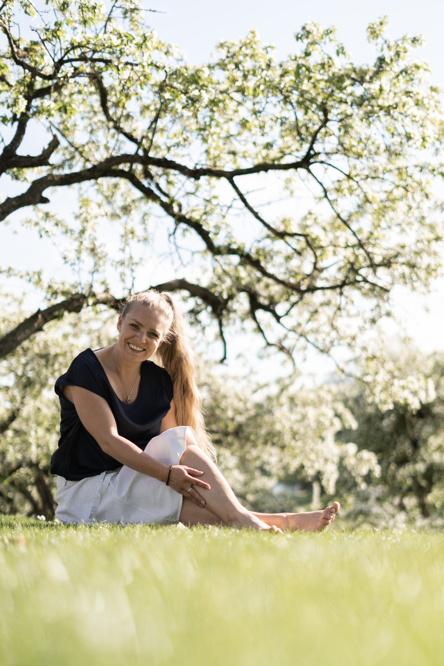 Frau sitzt während eines Fotoshootings im Frühling in München unter einen Baum der blüht
